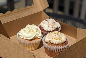 Three cupcakes with white frosting in a carry out box.